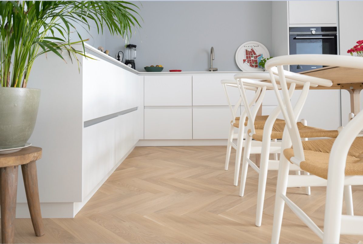 Fiskbensparkett Bauwerk Monopark Crema B-Protect® lagd på köksgolv. Vita köksmöbler, matbord och stolar.