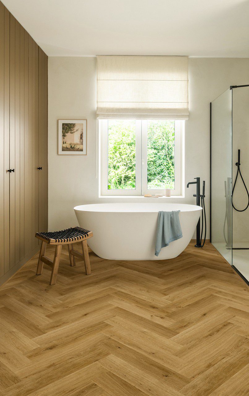 Herringbone laminate floor Quick-Step Impressive Design Cinnamon installed to bathroom floor. White separatly standind bathtub