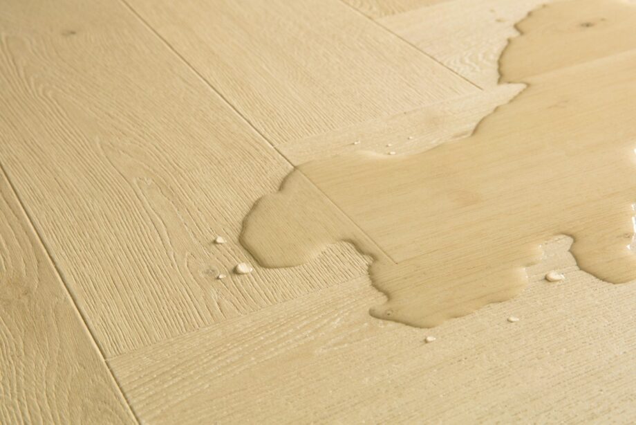 Kalanruoto laminaatti Quick Step Impressive Design Ginger Oak, lämmin keskiruskea tammen sävy ja tasainen lajitelma, vesilätäkkö osoittamassa vedenkestävyyttä