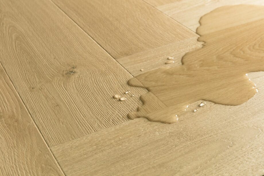 Kalanruotolaminaatti Quick Step Pergo Impressive Design Gardamom Oak, vaaleanruskea tammen sävy ja tasainen lajitelma, vesilätäkkö osoittamassa vedenkestävyyttä