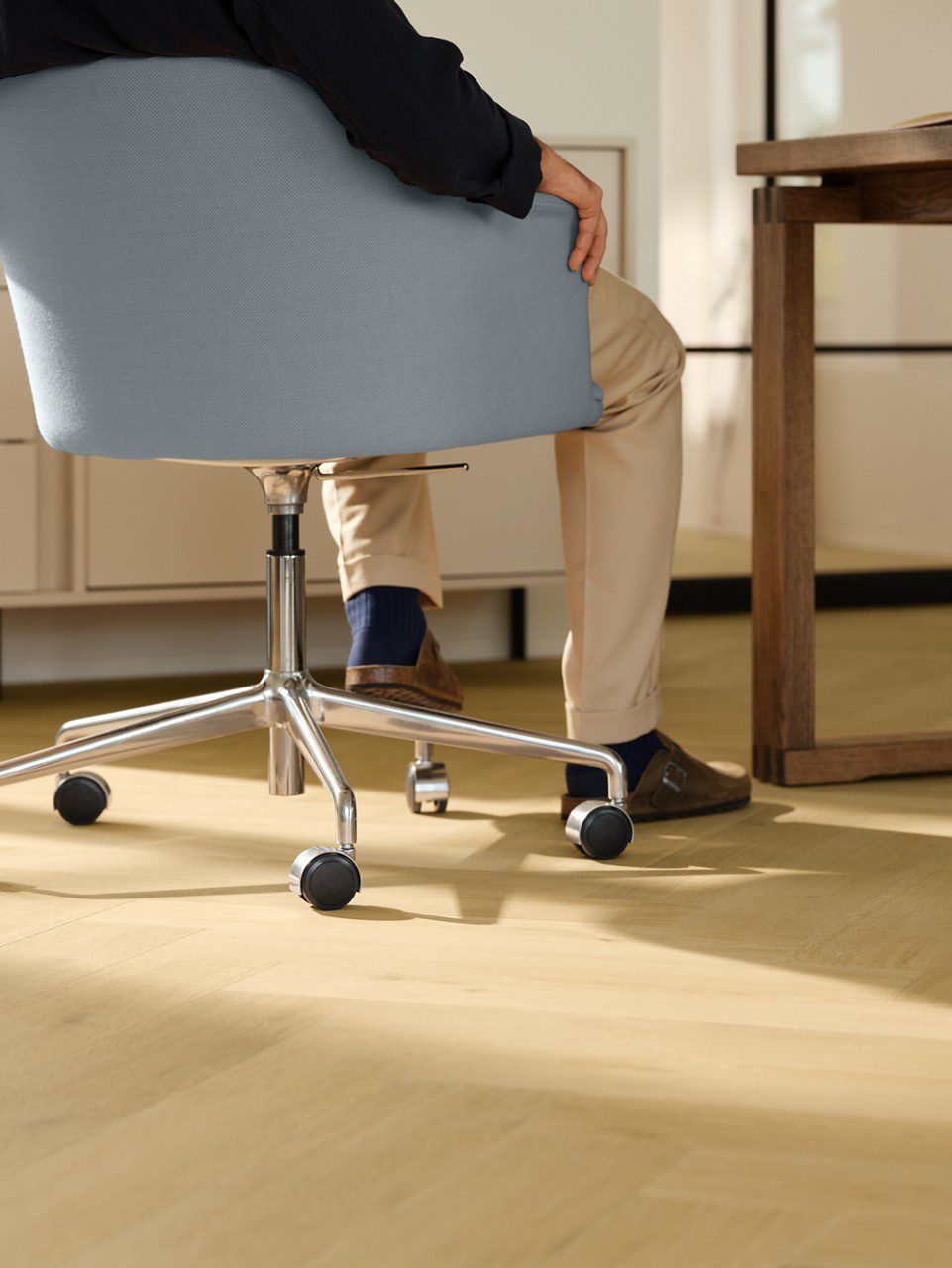 Laminat Quick Step Impressive Design Nutmeg Oak, verlegt im Büro, blauer Bürostuhl mit sitzendem Mann