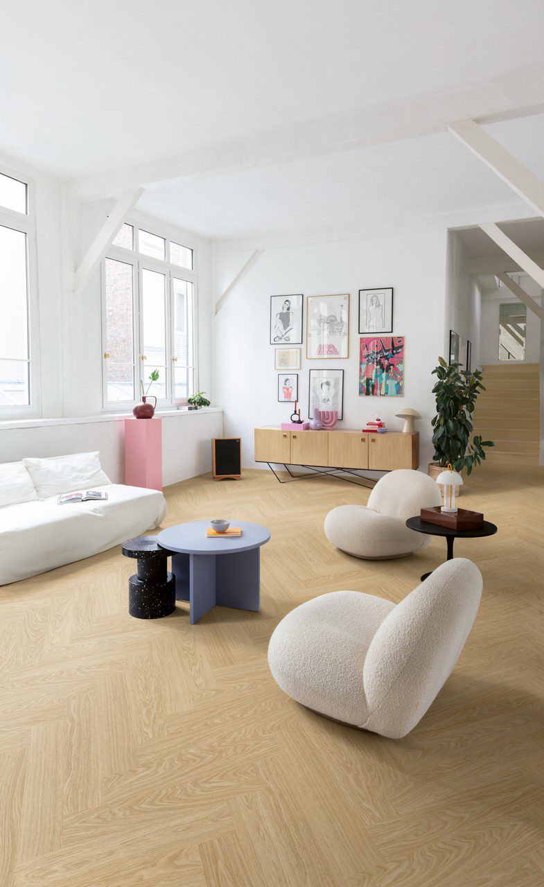 Виниловый ламинат Quick-Step Ciro Pure Oak Blush, уложен на полу и лестнице в гостиной с использованием плинтусов Incizo. Белый диван, белые кресла, небольшие круглые журнальные столики и комод.