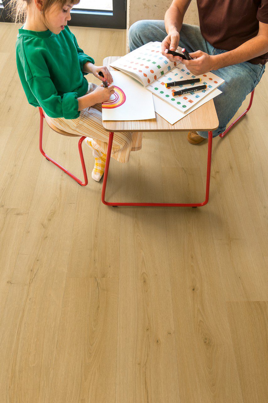 Klickvinyl Quick Step Bloom Brushed Oak Honey im Kinderzimmer verlegt, Tochter und Vater sitzen am Tisch und zeichnen.