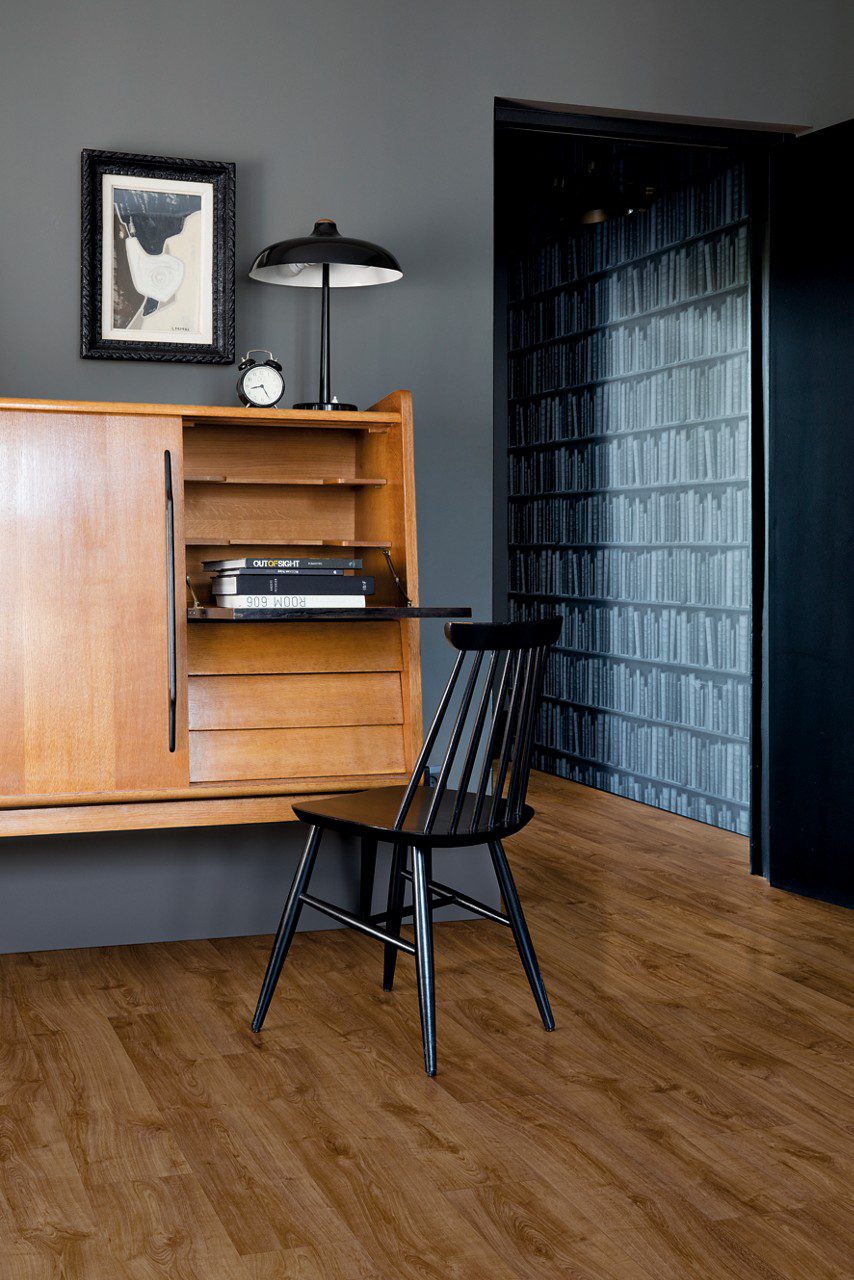 Quick Step Bloom Autumn Oak Brown LVT floor installed in an office, with a cabinet, chair and lamp.