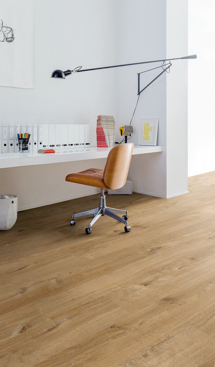 LVT floor Quick-Step Bloom Cotton Oak Natural installed on a home office floor. White office table, brown leather office stool and a lamp.