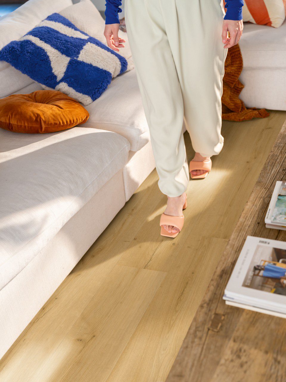 LVT flooring Quick-Step Bloom brushed oak honey installed on a livingroom floor. Woman walking on the floor, sofa and sofa table.