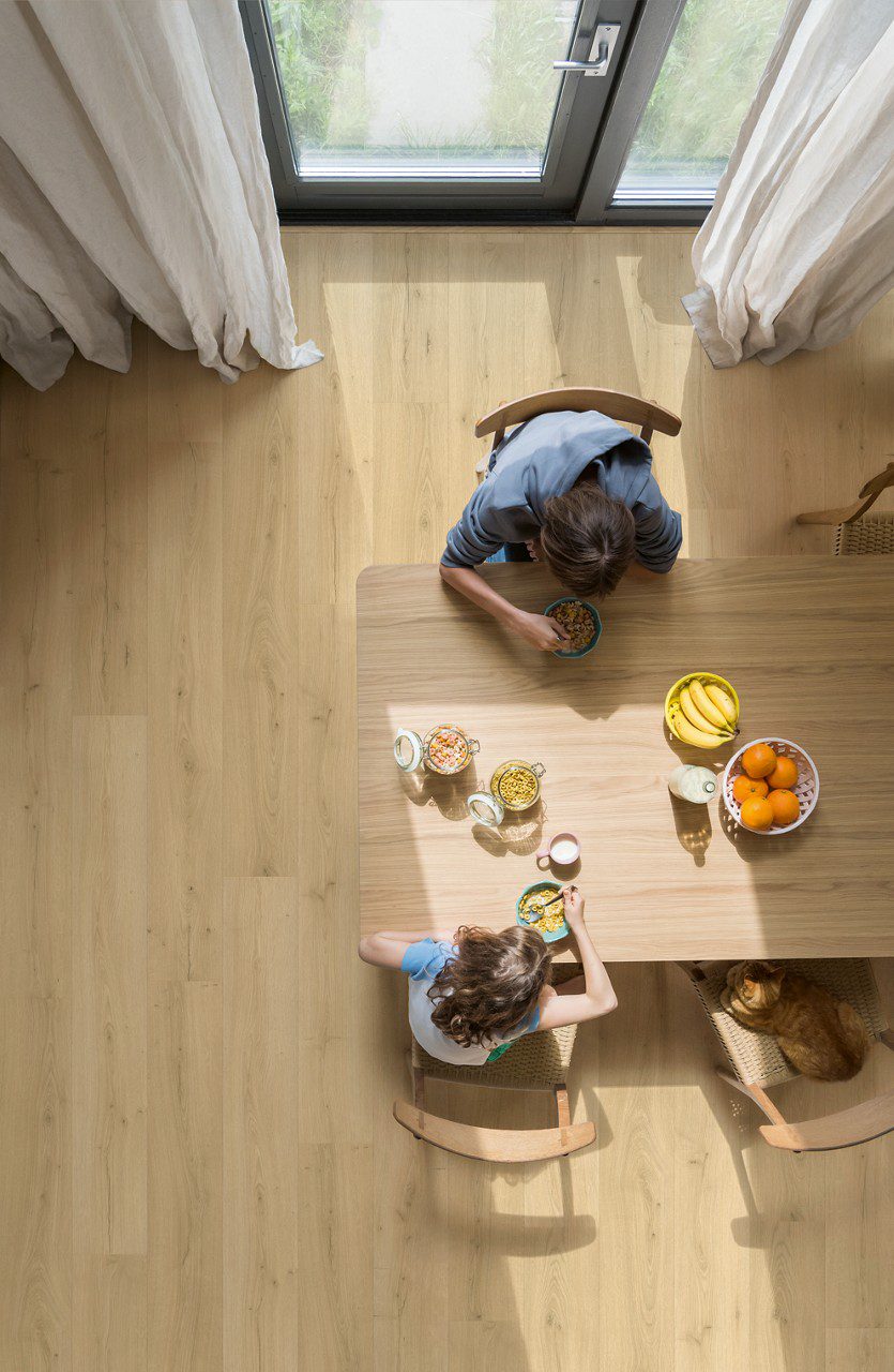 LVT parkett Quick Step Bloom Brushed Oak Beige paigaldatud söögitoa põrandale, söögilaud ja toolid, pere einestamas laua taga.