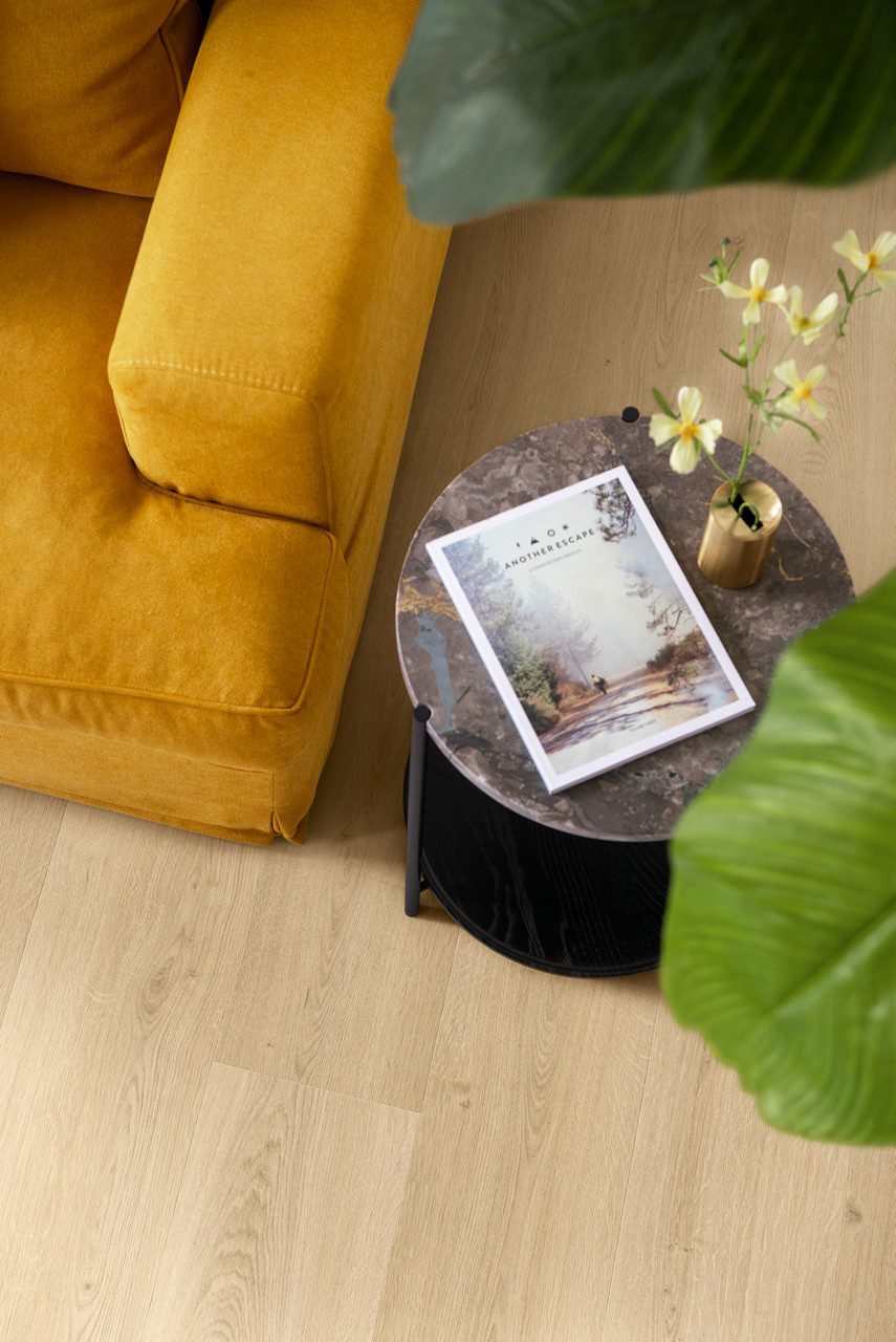 LVT põrand Quick Step Bloom Botanic Beige paigaldatud elutoa põrandale. Oranzh diivan, diivanilaud milell lilled ja ajakiri.