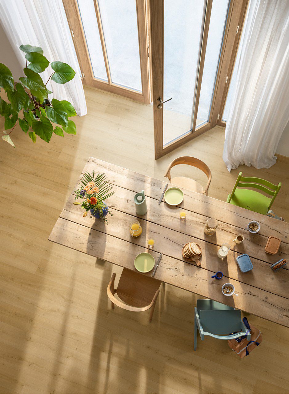 Rigid Vinylboden Quick Step Bloom Brushed Oak Honey im Esszimmer verlegt, Esstisch und Stühle, Blumen, Frühstück auf dem Tisch.