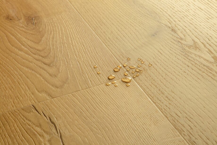 vinuulparkett-quick-step-bloom-brushed-oak-honey Vinüülparkett Quick-Step Bloom Brushed Oak Honey harjatud pind, soe tamme toon, veepiisad vinüülparketil näitamaks veekindlust.