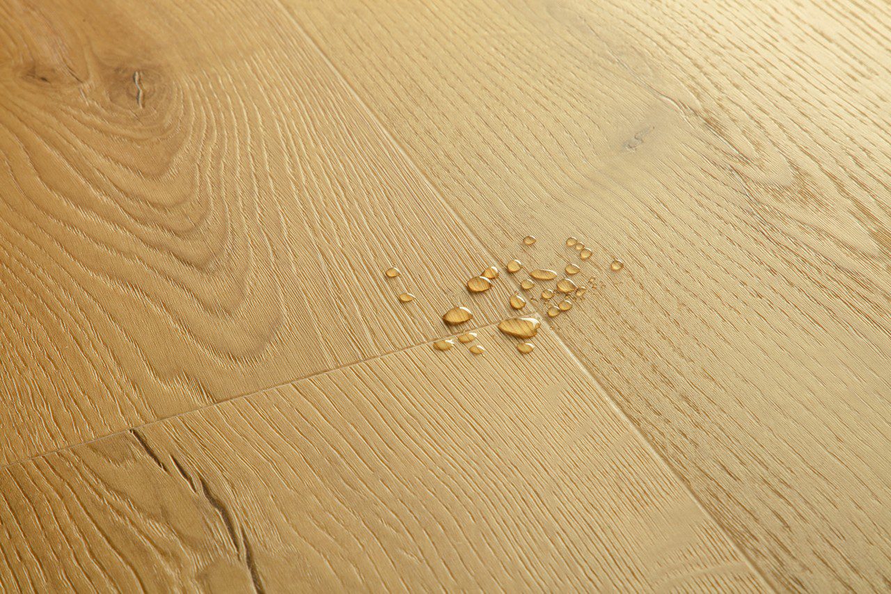 Vinüülparkett Quick-Step Bloom Brushed Oak Honey harjatud pind, soe tamme toon, veepiisad vinüülparketil näitamaks veekindlust.