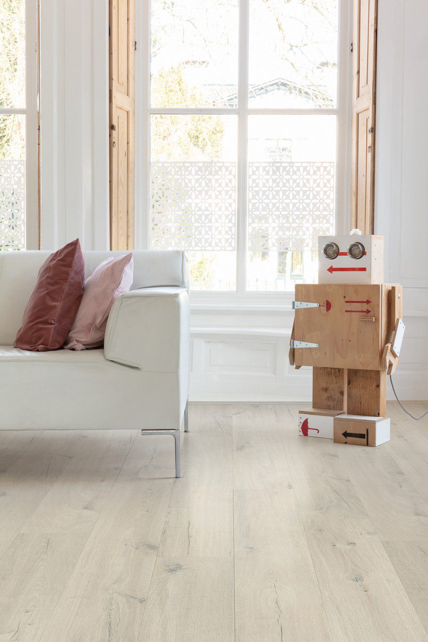 Vinüülparkett Quick-Step Bloom Cotton Oak White Blush paigaldatud elutoa põrandale. Puidust tehtud roboti makettm klassikalised aknad puidust aknakatetega.