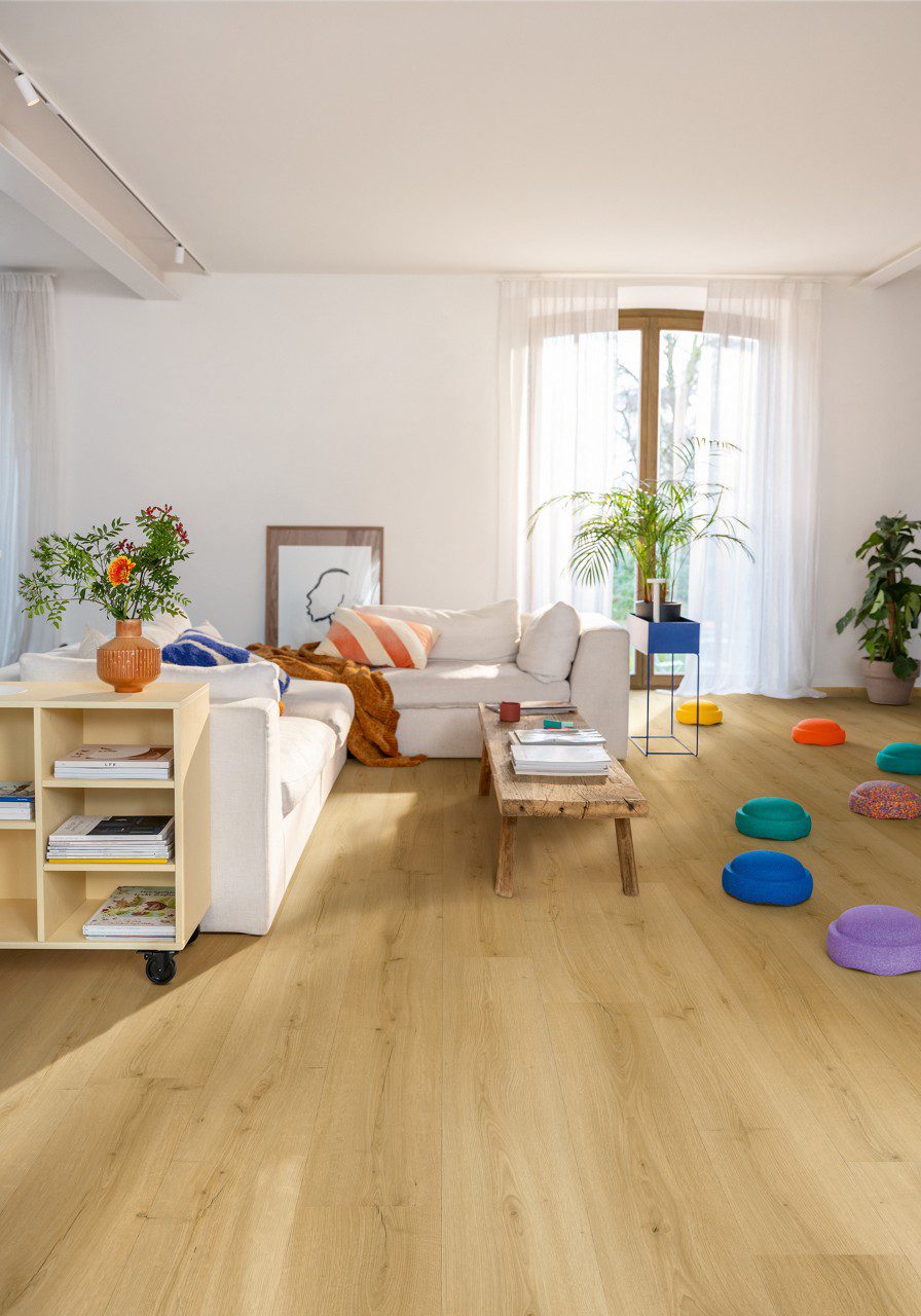 Vinyl floor Quick-Step Bloom Brushed Oak Honey installed on a living room floor. Sofa, table, flowers.