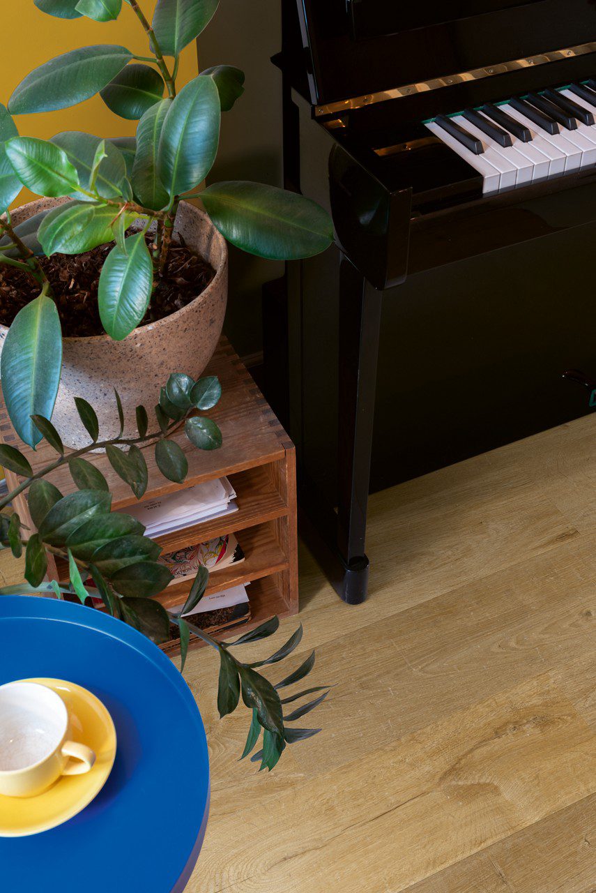 Vinyl floor Quick-Step Bloom Cotton Oak Natural installed in living floor, piano, blue table and flowers.