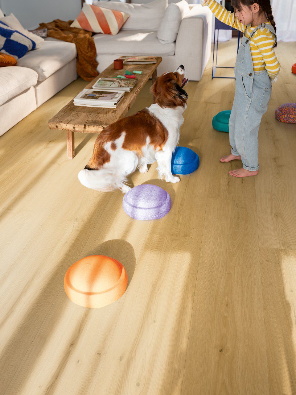 Vinylboden Quick Step Bloom Brushed Oak Honey im Wohnzimmer verlegt, Kind spielt mit einem Hund.