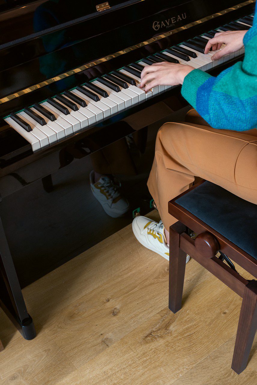 Vinyylilattia Quick Step Bloom Cotton Tammi Natural asennettuna olohuoneen lattialle, luonnollinen tammen sävy ja lankkudesign, joku soittaa pianoa.