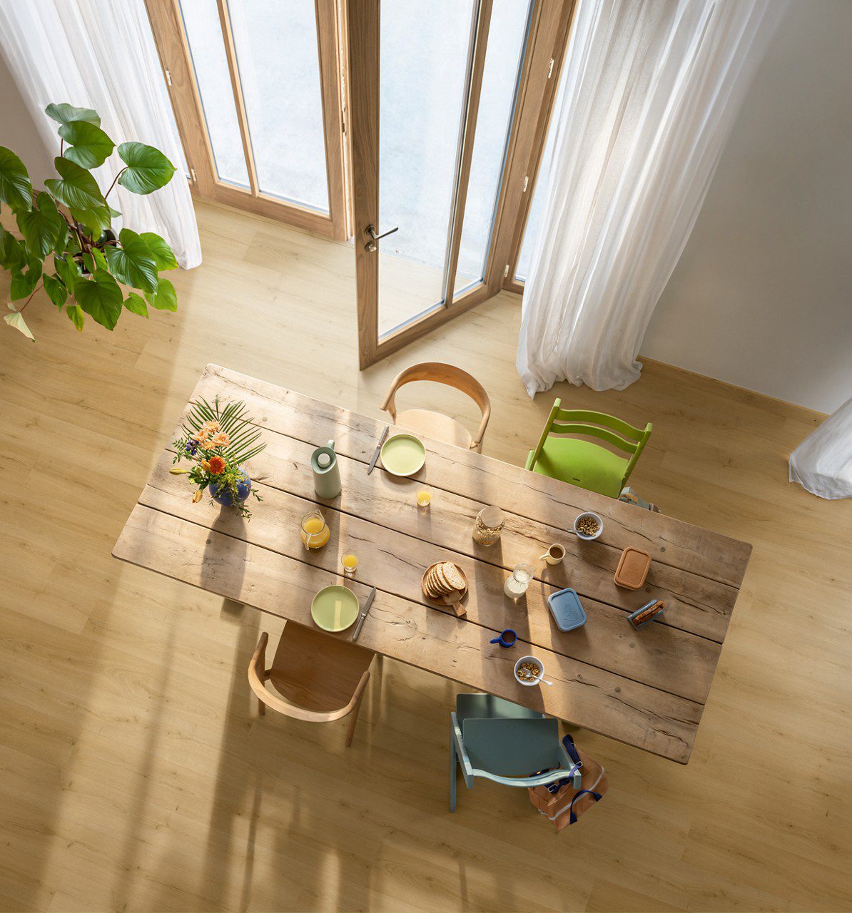 Виниловый паркет Quick Step Bloom Brushed Oak Honey уложен на полу на кухне, обеденный стол со стульями и открытая дверь на террасу.