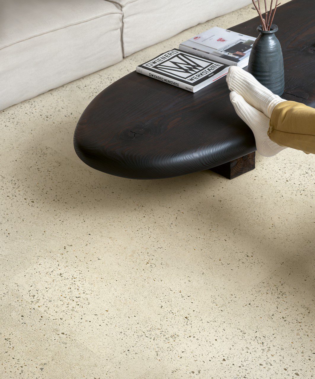 LVT põrand Quick-Step Illume Pubble concrete paigaldatud elutoa põrandale. Madal telekalaud milelel keegi toetab oma jalgu. Laual on lisaks jalgadele ka raamatud ja vaas.