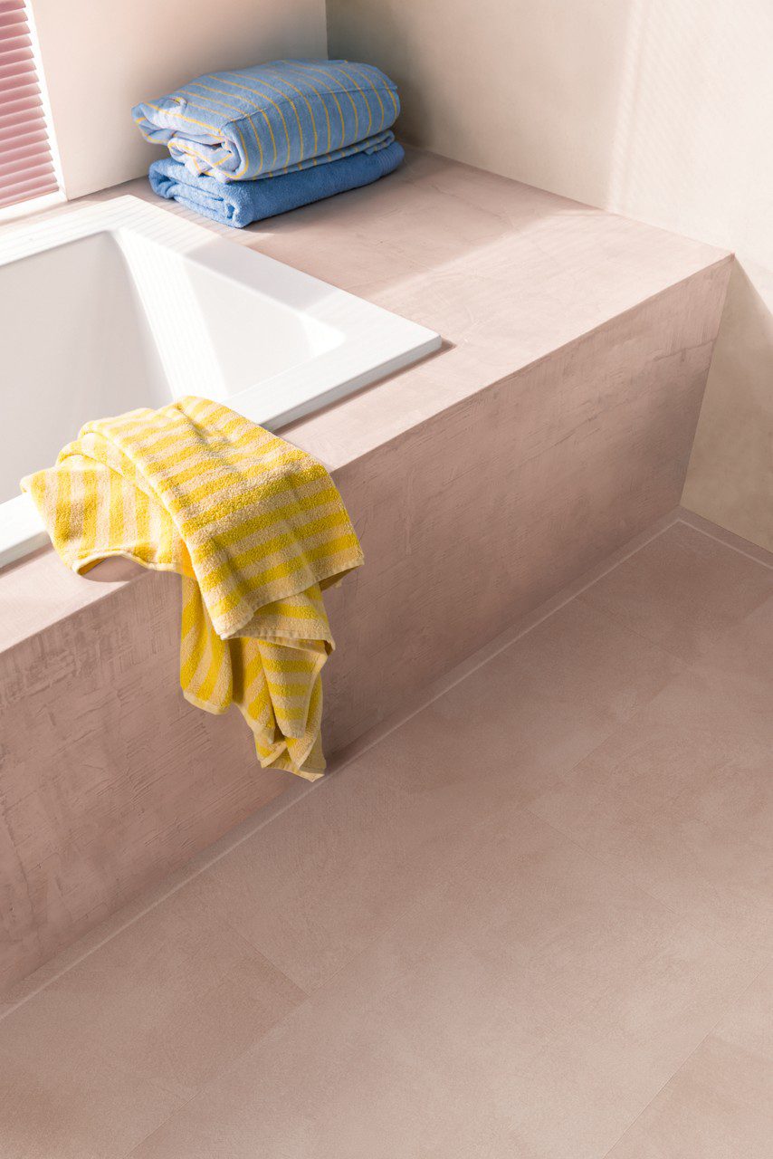 Vinyl flooring tiles Quick-Step Illume Soft blush installed on bathroom floor. Built in bath inside pink color structure same as flooring.