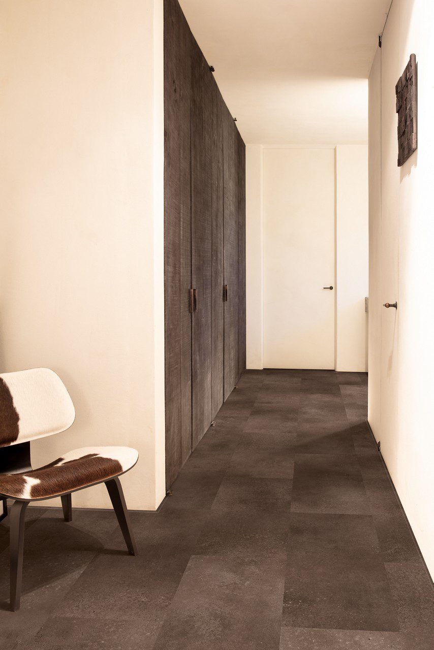 Vinyl flooring tiles Quick-Step Oro Cinnamon rock with dark brown bevelled natural stone flooring design. Installed on a hallway floor. Cow leather stool, integrated hallway closet.