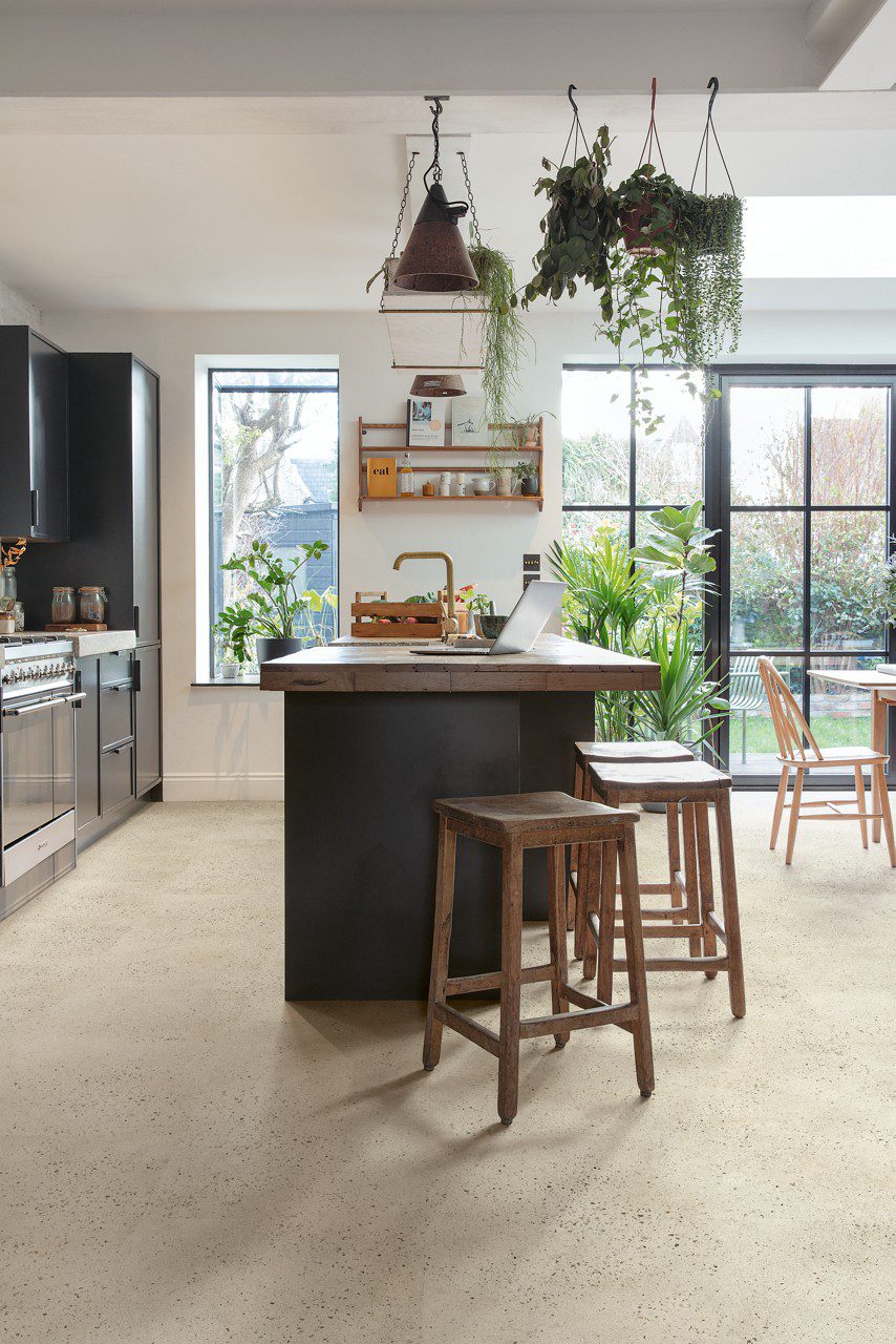 Vinyl tiles Quick-Step Illume Pebble concrete installed on a kitchen floor. Kitchen furniture with an island, rustical style stools next to it.
