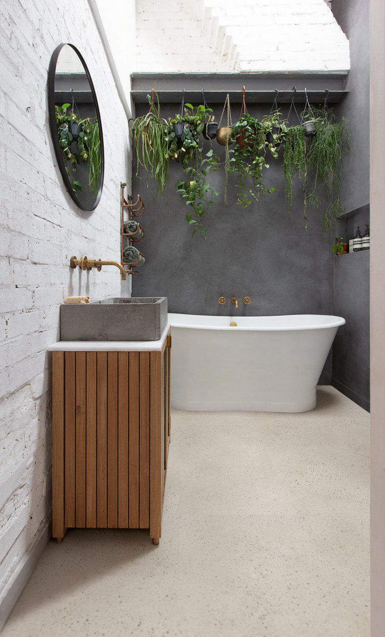 Vinylboden in Betonoptik Quick-Step Illume Oyster Concrete, verlegt im klassisch eingerichteten Badezimmer – freistehende Badewanne, Badmöbel mit Aufsatzwaschbecken auf Betonplatte sowie Wandarmaturen und Wannenmischer in Bronzeton.