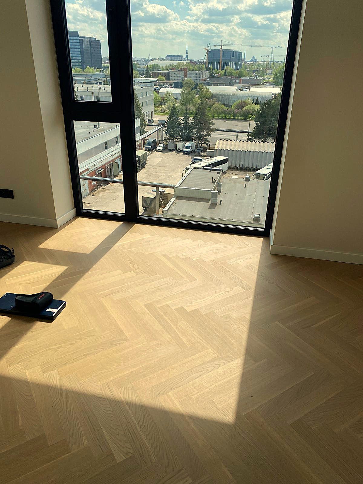 Fiskbensparkett Bauwerk Monopark ek Natur 15 Avorio lagd i ett rum med golvhögt fönster och solljus på golvet
