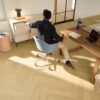 herringbone-laminate-floor-quick-step-impressive-design-nutmeg-oak Herringbone laminate floor Quick-Step Impressive Design Nutmeg Oak installed on office floor. Guy sitting at blue chair working at office desk, laptop.