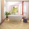 Laminat Fischgrät Quick Step Impressive Design Ginger Oak, verlegt im Badezimmerboden, freistehende weiße Badewanne, mit blauer Mosaikfliese verkleideter Sockel und rote Fensterrahmen