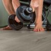 Klick Vinylboden Quick Step Bloom Cotton Oak Cozy Grey im Homegym verlegt, ein Mann hebt eine Hantel.