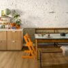 Vinylboden Quick Step Bloom Botanic Caramel Oak im Esszimmer verlegt, orangefarbener Kinderstuhl, Esstisch, Schränke und Blumen.