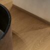 Vinyylilattia Quick Step Blos Cocoa Tammi asennettuna kylpyhuoneen lattialle, tumma kaakaonruskea tammen sävy ja lankkulattia tammi, samansävyiset jalkalistat ja musta luonnonkivinen kylpyamme.