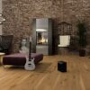 naturaalne-parkett-bauwerk-casapark-budget-cut-tamm-56-harjatud-matt-lakk-138mm Naturaalne parkett Bauwerk Casapark Budget Cut tamm 56 faasitud 2k, harjatud 138mm paigaldatud elutoa põrandale. Vana tellisest sein, küdev kamin, diivan, diivanilaud, pehme suur tumba mille najal kitarr koos võimendiga.