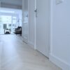 Vit fiskbensparkett Bauwerk Monopark ek Natur 15 Farina i hallen Fiskbensparkett Bauwerk Monopark ek Natur 15 Farina lagd i en hall med vita dörrar och golvlister, vardagsrum i bakgrunden